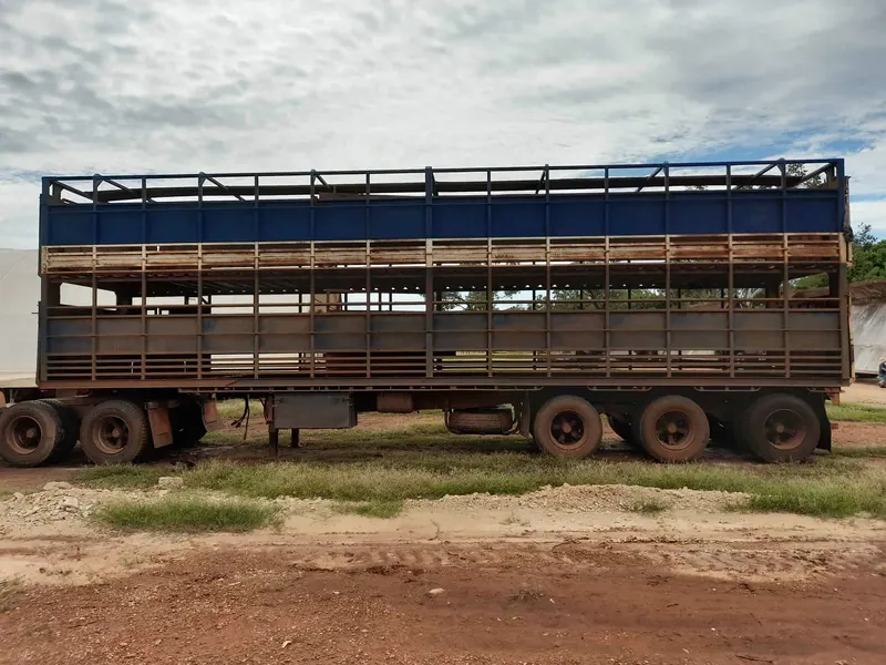 A triple-deck livestock trailer parked on open ground